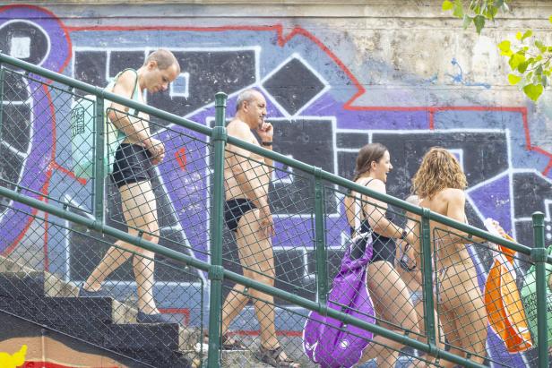 Menschen in Badebekleidung gehen eine Stiege hinab - entlang einer Mauer voll mit Graffiti-Schriftzügen.
