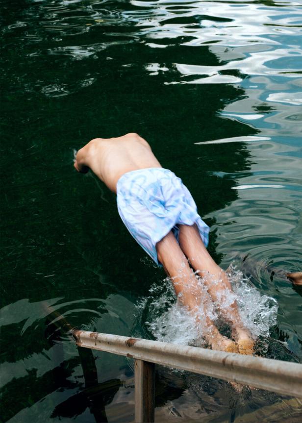 Eine Person springt mit dem Kopf voran in einen dunklen See.