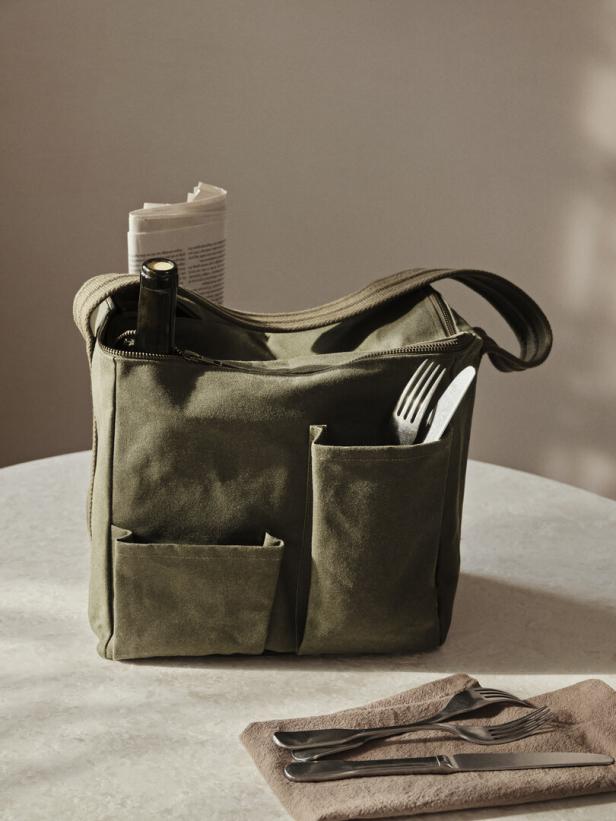 Eine grüne Tasche mit Weinflasche, Zeitung und Besteck auf einem Tisch.