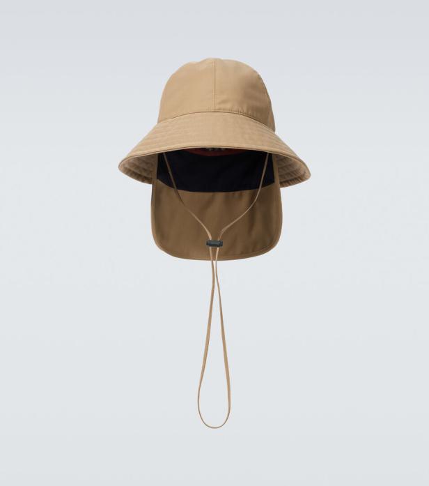 Ein beiger Fischerhut mit Nackenschutz und Kinnband vor einem hellen Hintergrund.