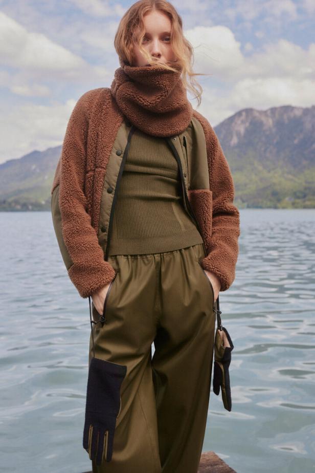 Eine Frau in Outdoor-Kleidung steht vor einem See und Bergen.