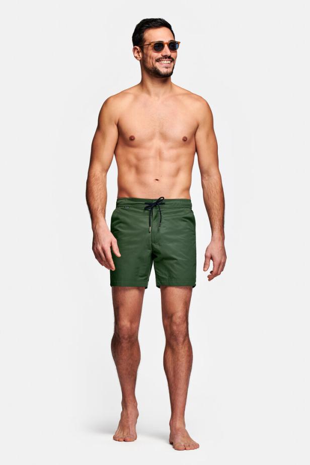 Ein Mann mit Sonnenbrille und grüner Badehose steht vor einem weißen Hintergrund.