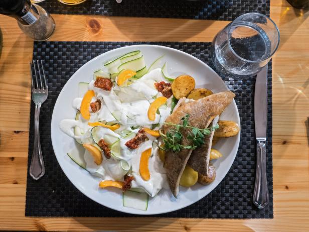 Ein Teller mit Fisch, Kartoffeln, Zucchini und einer hellen Soße auf einem Tisch.