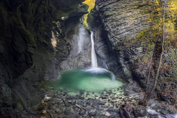 Ein Wasserfall ergießt sich in einen smaragdgrünen See, umgeben von steilen Felswänden.