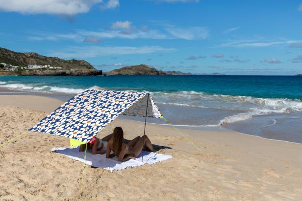 Zwei Frauen liegen unter einem Sonnenschutz am Strand.