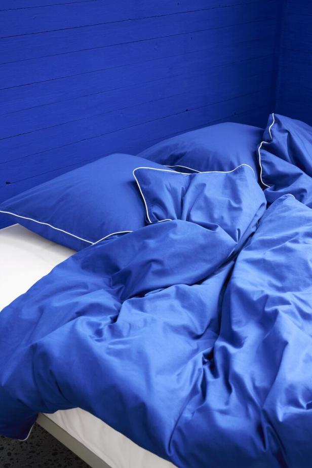 Ein blaues Bett mit weißem Rand vor einer blauen Holzwand.