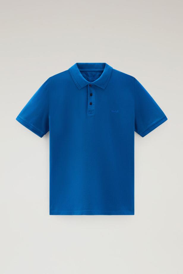 Ein blaues Poloshirt mit drei Knöpfen liegt auf einem weißen Hintergrund.
