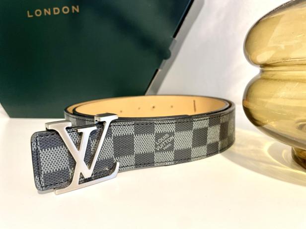 Ein karierter Louis Vuitton Gürtel mit silberner Schnalle liegt auf einem Tisch.