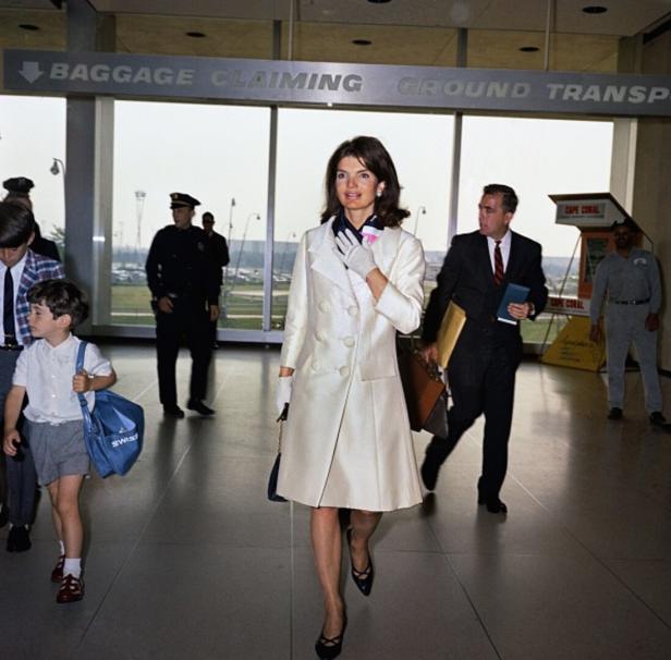 Jackie Kennedy geht mit ihrem Sohn auf einem Flughafen entlang.