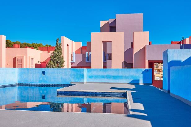 Eckige Gebäude in rosa und blauen Pastelltönen – davor ein gekachelter Pool.
