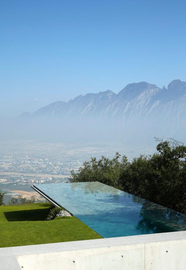 Von der Terrasse hebt sich ein Infinity-Pool ab, im Hintergrund stehen Berge, darunter liegt eine Wüstenstadt.