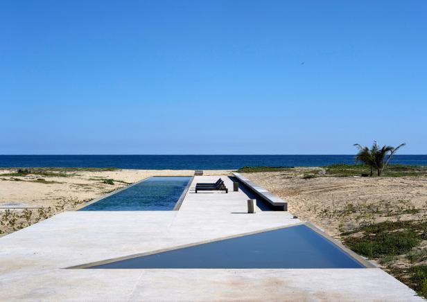 Eine betonierte Terrasse auf einem einsamen Strand. In sie sind zwei Becken eingelassen, ein rechteckiges und eines, das ein Dreieck bildet.