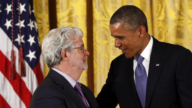 George Lucas und Barack Obama stehen zusammen vor einer US-Flagge.
