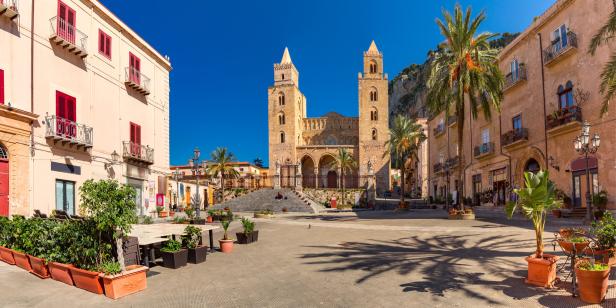 Panorama des Doms von Monreale in Sizilien, umgeben von historischen Gebäuden und Palmen.