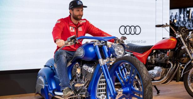 Ein Mann sitzt auf einem blauen Motorrad vor einem Audi- und Ski World Cup-Hintergrund.
