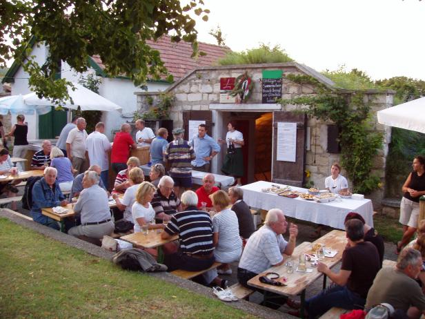 Viele Menschen sitzen an Tischen vor einem Heurigen und genießen die Zeit.