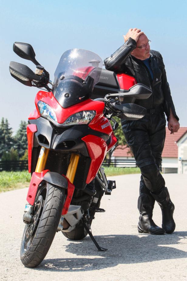 Ein Mann in Lederkleidung lehnt an einem roten Ducati-Motorrad.
