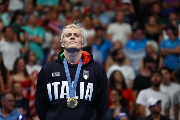 Ein italienischer Schwimmer mit blonden Haaren und einer Goldmedaille vor einer Zuschauermenge.
