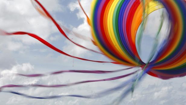 Ein bunter Drachen mit flatternden Bändern vor einem Himmel mit Wolken.