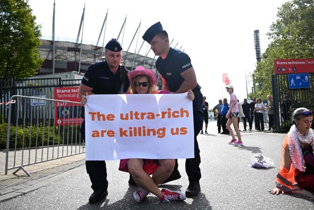 Polizisten tragen eine Demonstrantin mit einem Schild, auf dem steht: „Die Superreichen bringen uns um“.
