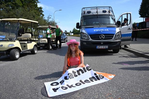 Eine junge Frau sitzt mit einem Transparent der „Ostatnie Pokolenie“ vor einem Polizeiwagen auf der Straße.
