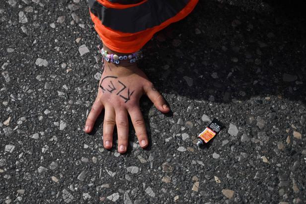 Die Hand einer Person mit aufgemalter Aufschrift und ein Tube Sekundenkleber liegen auf dem Asphalt.