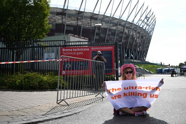 Eine Frau sitzt vor dem Nationalstadion Warschau und hält ein Protestplakat.