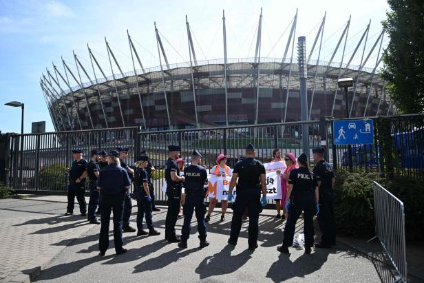 Eine Gruppe Polizisten steht vor dem Nationalstadion in Warschau, während Demonstranten protestieren.