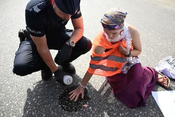 Ein Polizist beobachtet eine Aktivistin, die ihre Hand auf eine mit Flüssigkeit bedeckte Straße legt.
