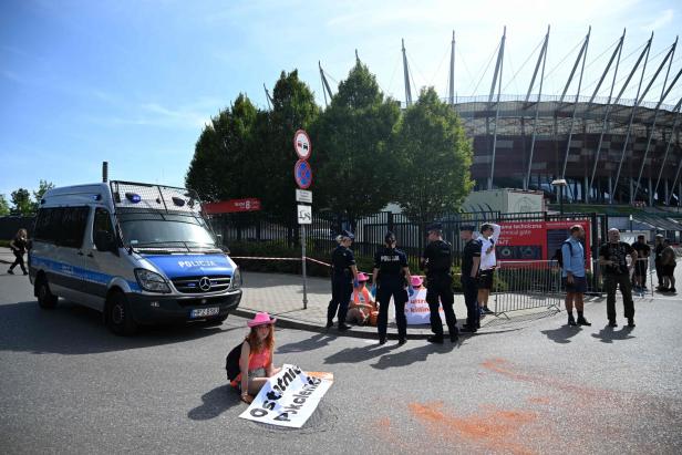 Vor dem Nationalstadion in Warschau demonstriert eine Aktivistin der „Letzten Generation“ vor einem Polizeiwagen.
