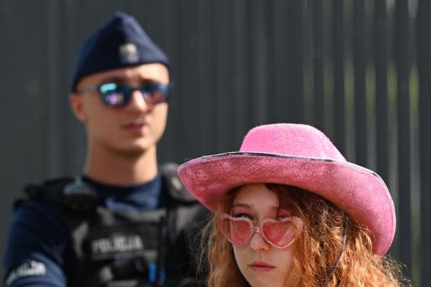 Eine junge Frau mit rosa Cowboyhut und Herzchenbrille steht vor einem Polizisten.
