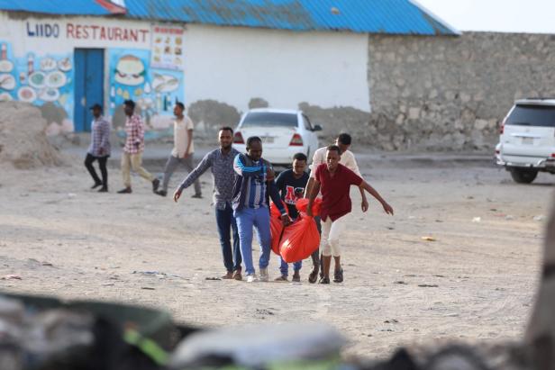 SOMALIA-UNREST Eine Gruppe von Männern trägt rote Säcke durch eine staubige Straße.