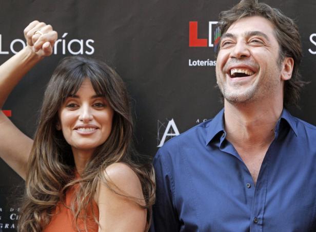 Penélope Cruz und Javier Bardem posieren lächelnd vor einer Wand mit Logos.
