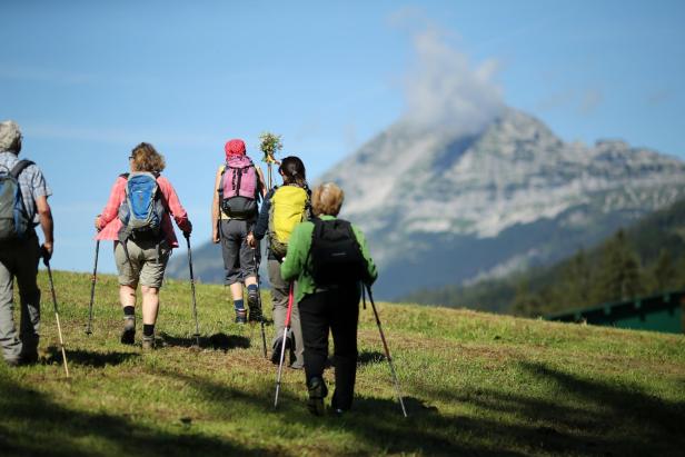 Eine Gruppe Wanderer geht auf einem grasbewachsenen Hügel in Richtung eines Berges.