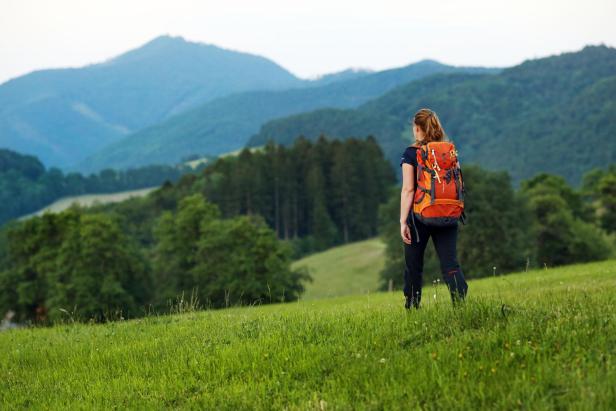 Eine Frau mit Rucksack wandert in einer grünen Hügellandschaft.