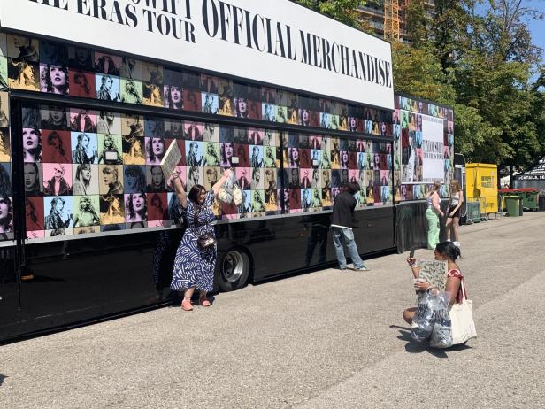 Eine Frau macht ein Foto von einer anderen Frau vor einer Taylor-Swift-Plakatwand