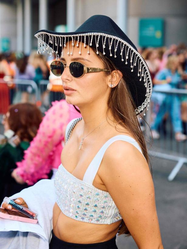 Eine Frau mit Sonnenbrille und Cowboyhut mit Strassfransen vor einer Menschenmenge.