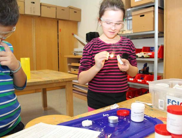 Ein Mädchen mit Schutzbrille zündet ein Streichholz an.