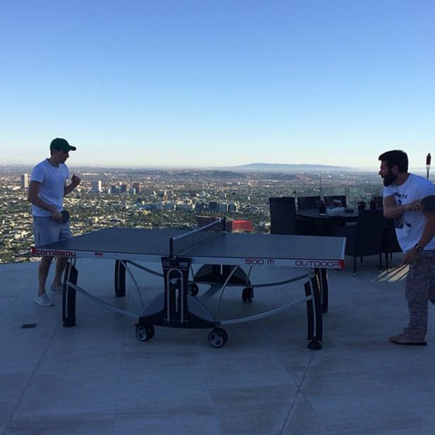 Zwei Männer spielen Tischtennis auf einer Dachterrasse mit Blick auf die Stadt.