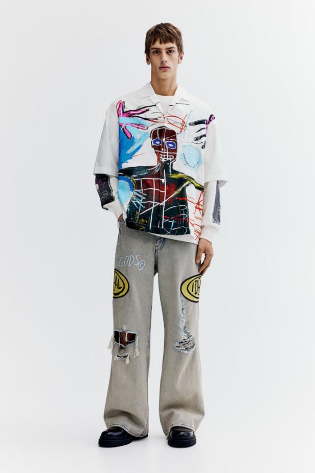 Ein Mann trägt ein Hemd mit einem Kunstwerk und zerrissene Jeans mit Flicken.