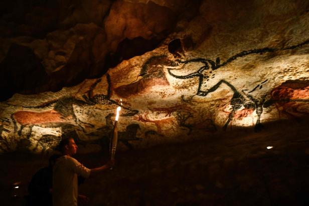 Ein Mann leuchtet mit einer Fackel auf die Höhlenmalereien von Lascaux.