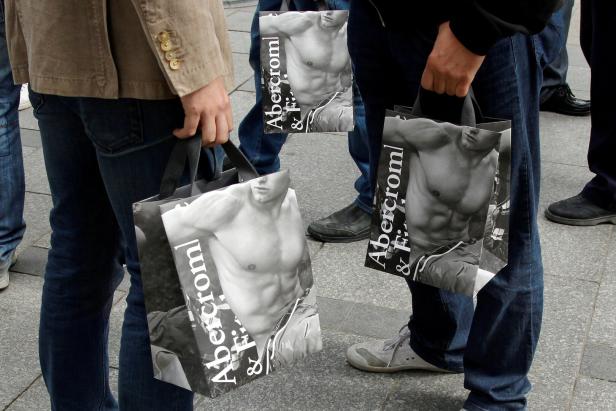 Mehrere Personen tragen Einkaufstüten von Abercrombie & Fitch mit dem Bild eines Mannes mit freiem Oberkörper.
