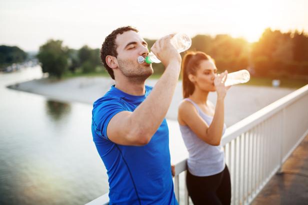 Ein Mann und eine Frau trinken Wasser nach dem Sport auf einer Brücke.