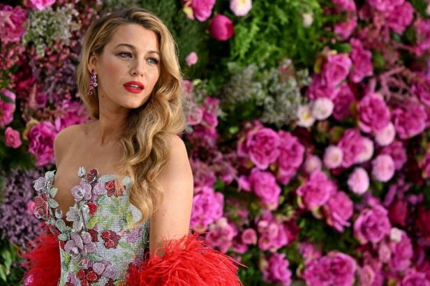 Blake Lively posiert vor einer Wand aus rosa und grünen Blumen.
