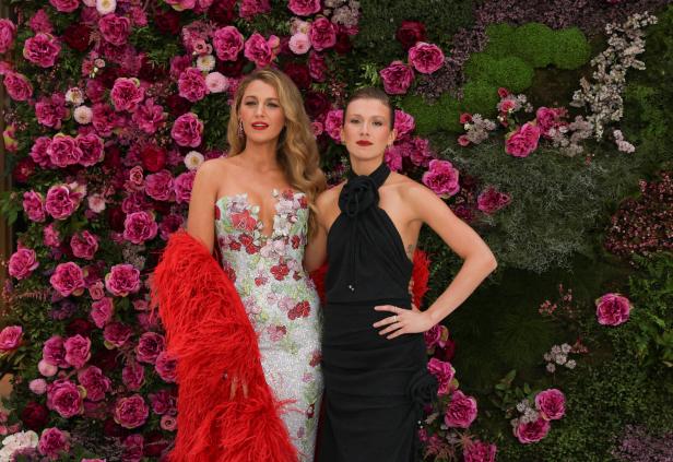 Zwei Frauen posieren vor einer Wand aus Blumen und Pflanzen.