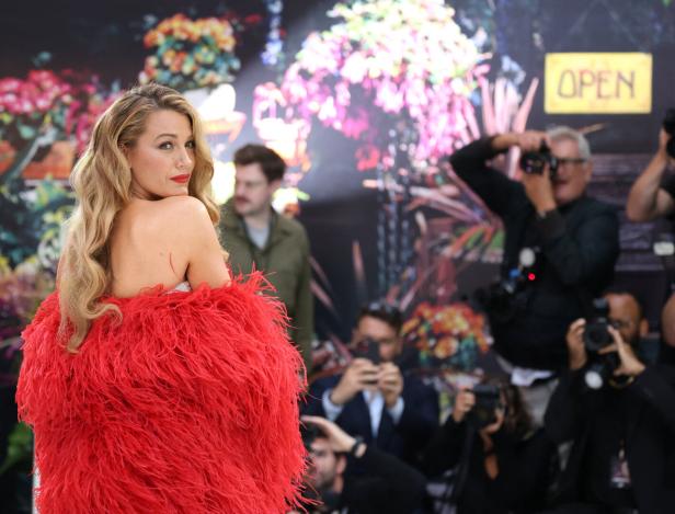 Blake Lively posiert in einem roten Federkleid vor einer Blumenwand für Fotografen.