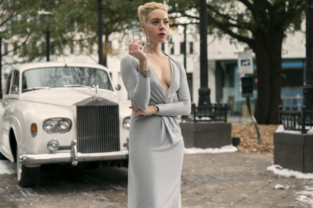 Eine Frau im grauen Kleid raucht vor einem weißen Rolls-Royce.