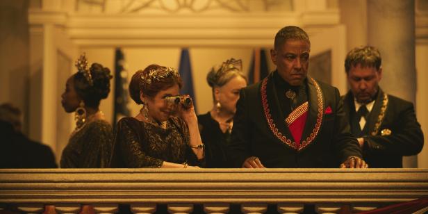 Giancarlo Esposito und andere Schauspieler auf einem Balkon, eine Frau schaut durch ein Fernglas.