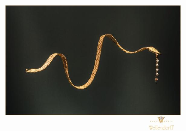 Ein goldenes Wellendorff-Armband mit Perlenanhänger vor dunklem Hintergrund.