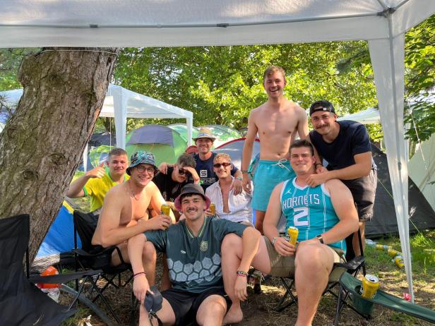 Neun Festivalbesucher ausgerüstet mit Bier und Sonnenhut unter ihrem Pavillon.